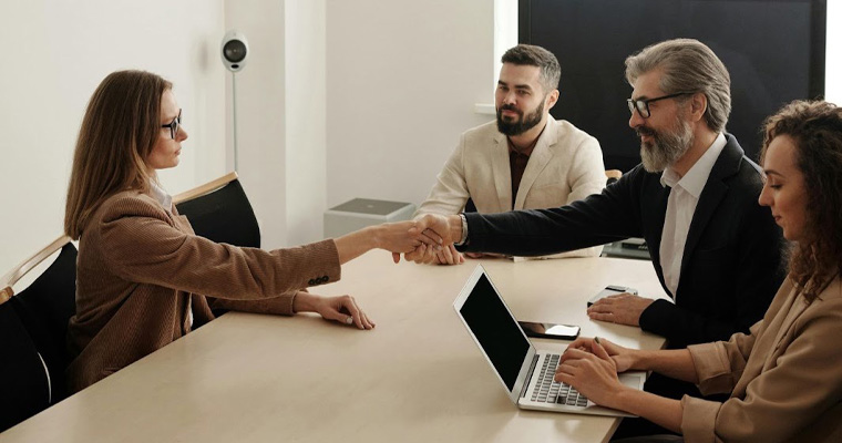 A woman and man shake hands at a business meeting.