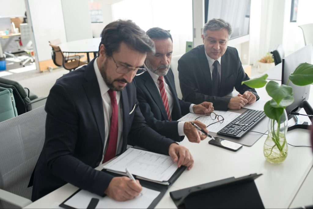 An IP docket specialist writes in his notebook next to two office workers.